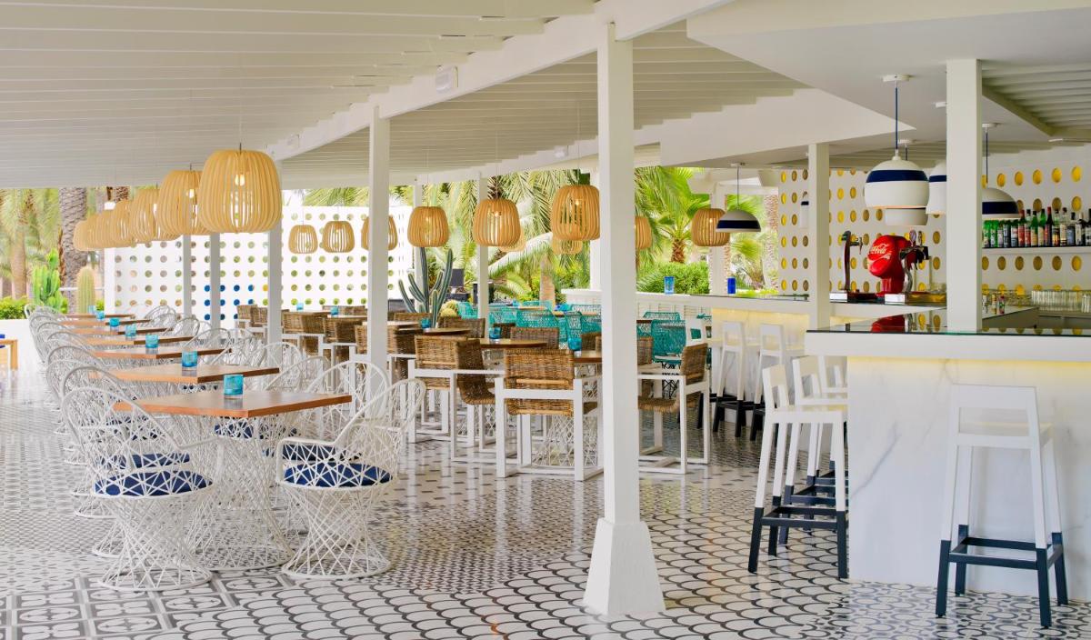 Un restaurante con sillas y mesas blancas y un bar. en Boutique Hotel H10 Big Sur - Adults Only, en Los Cristianos