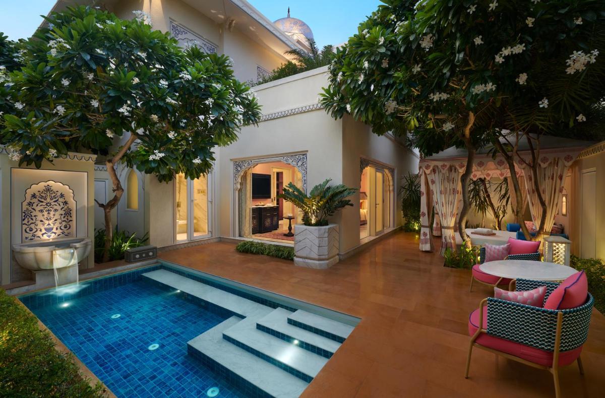 a house with a swimming pool in the middle of a yard at The Leela Palace Jaipur in Jaipur