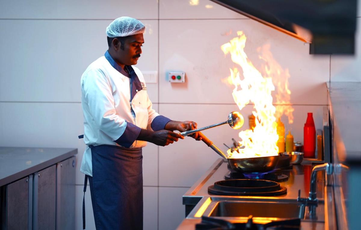 a man cooking in a pot on a stove with flames at Elephant Passage in Munnar