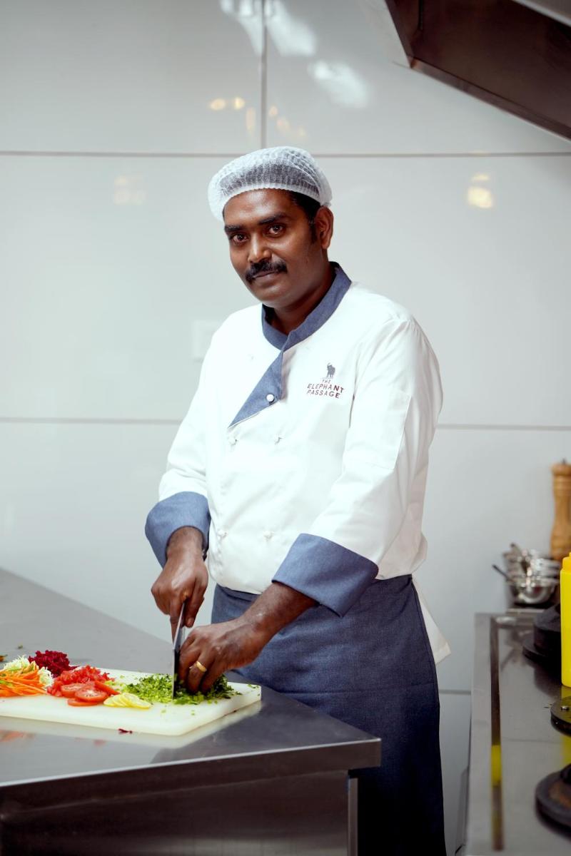 a man in a kitchen cutting a plate of food at Elephant Passage in Munnar