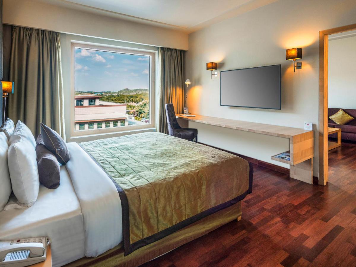 a hotel room with a bed and a desk and a window at Novotel Hyderabad Airport in Hyderabad