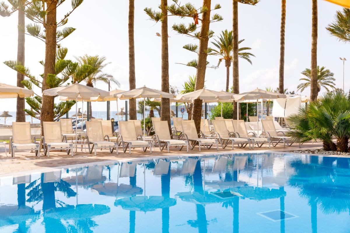 una piscina con sillas y sombrillas y palmeras en CM Playa del Moro, en Cala Millor