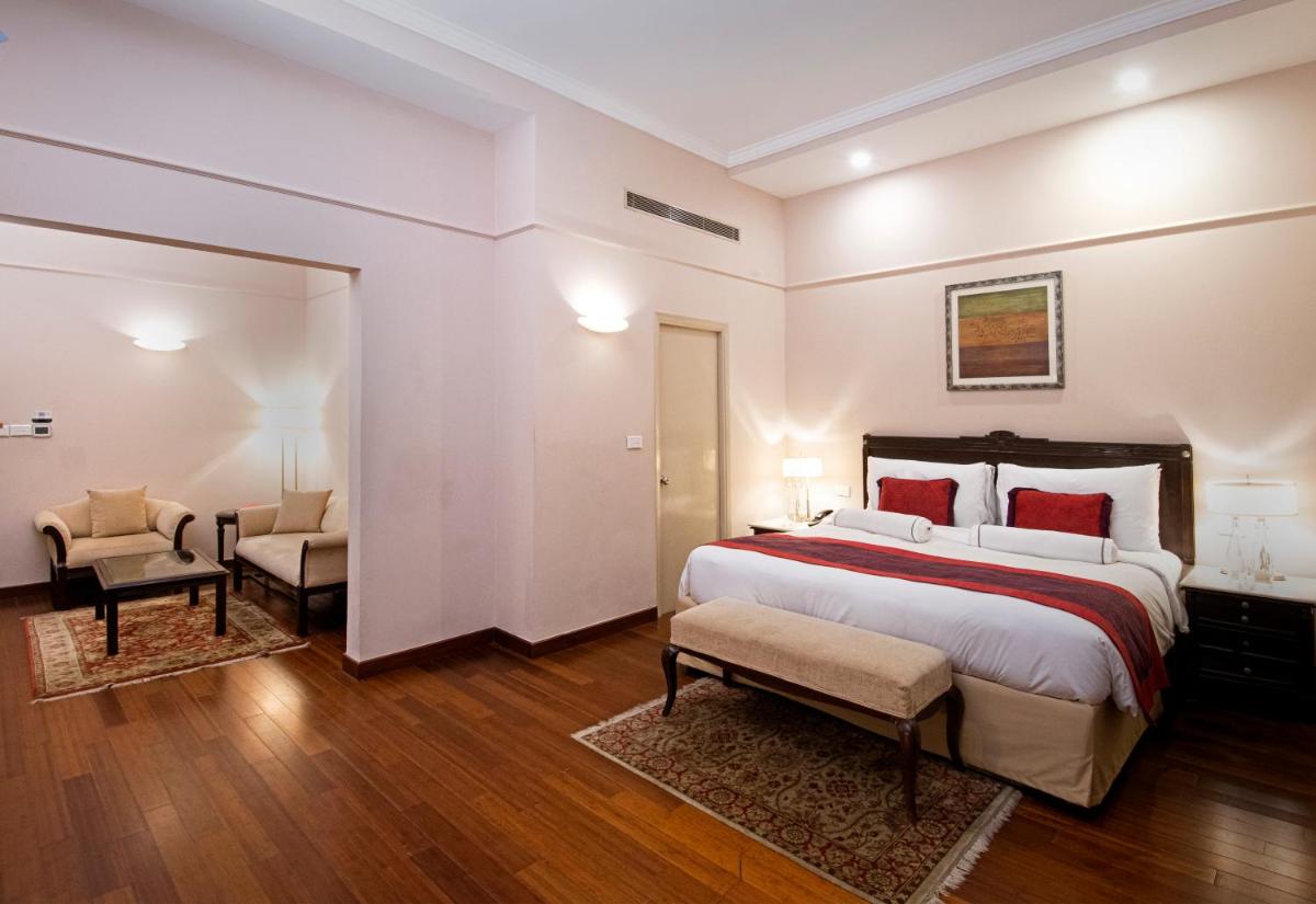 a bedroom with a large bed and two chairs at The Claridges New Delhi in New Delhi a bedroom with a large bed and two chairs at The Claridges New Delhi in New Delhi