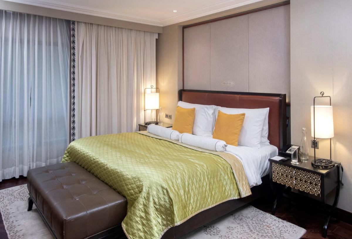 a hotel room with a large bed with yellow pillows at The Claridges New Delhi in New Delhi a hotel room with a large bed with yellow pillows at The Claridges New Delhi in New Delhi