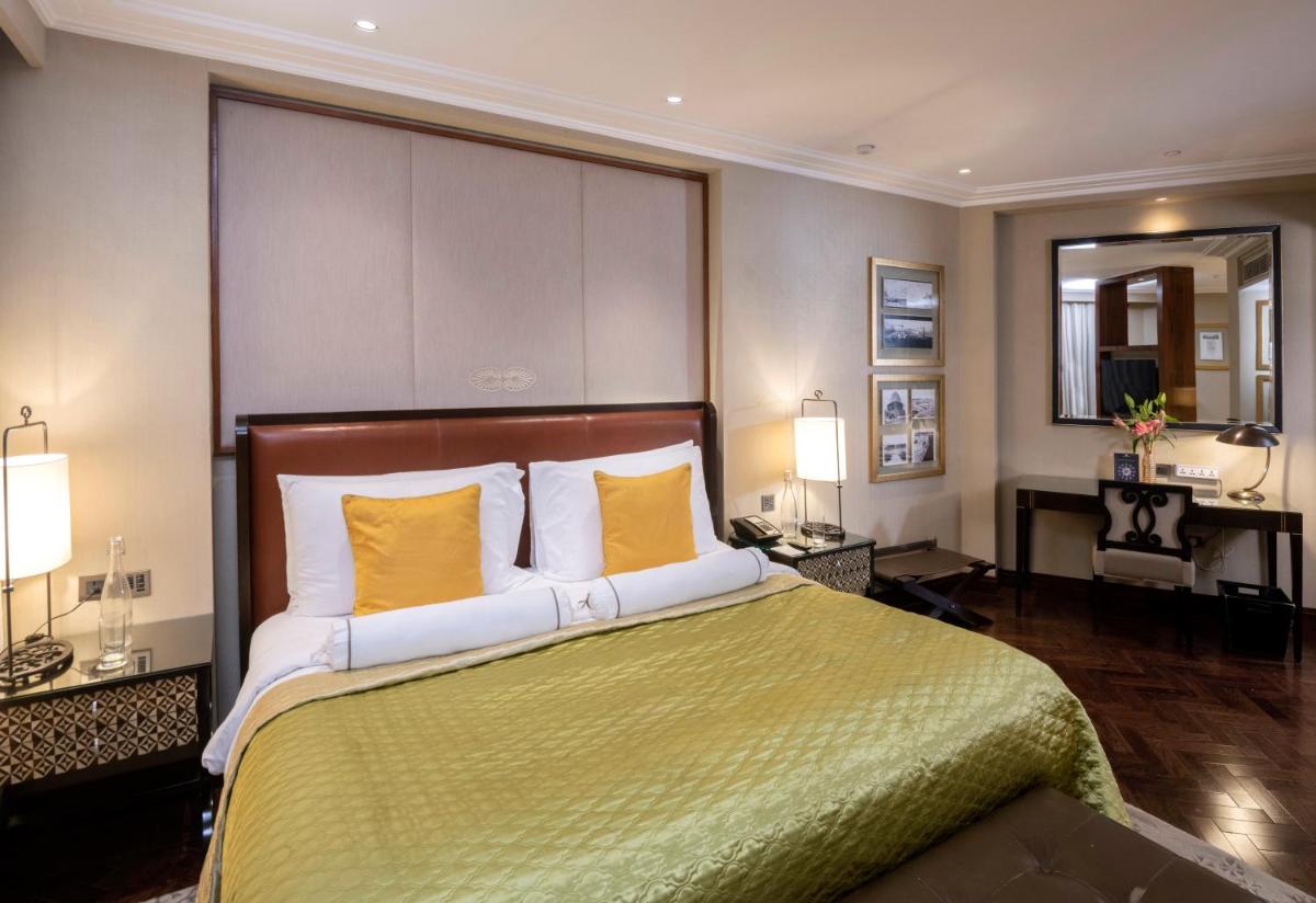 a bedroom with a large bed with yellow pillows at The Claridges New Delhi in New Delhi a bedroom with a large bed with yellow pillows at The Claridges New Delhi in New Delhi