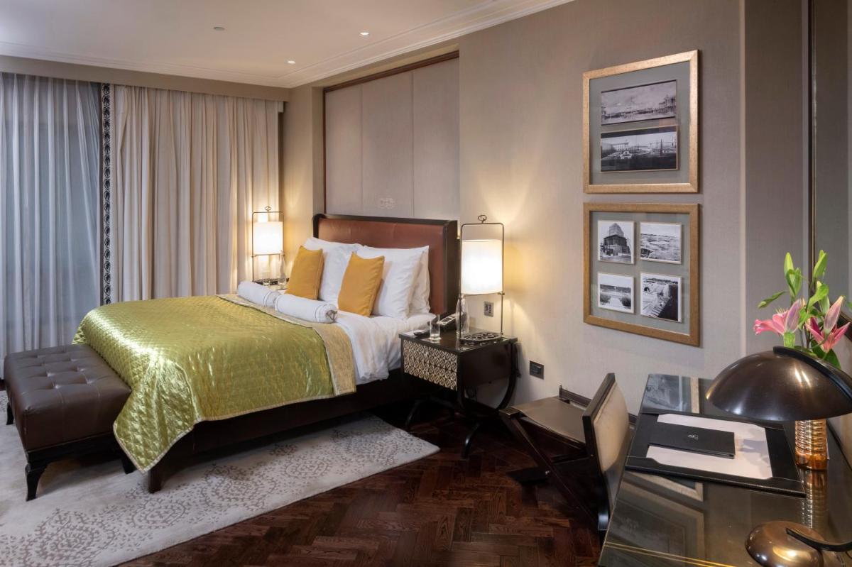 a hotel room with a bed and a desk and lamps at The Claridges New Delhi in New Delhi a hotel room with a bed and a desk and lamps at The Claridges New Delhi in New Delhi