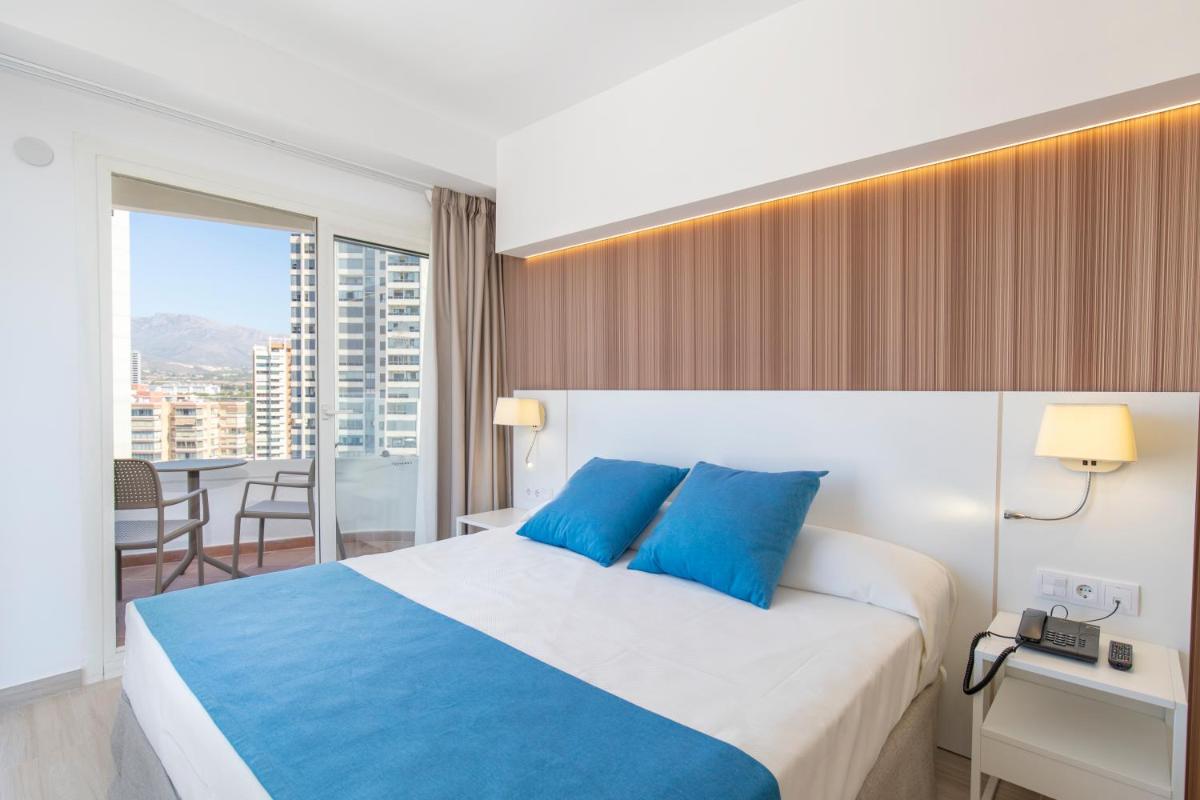 Una habitación de hotel con una cama grande con almohadas azules. en Hotel Rosamar, en Benidorm