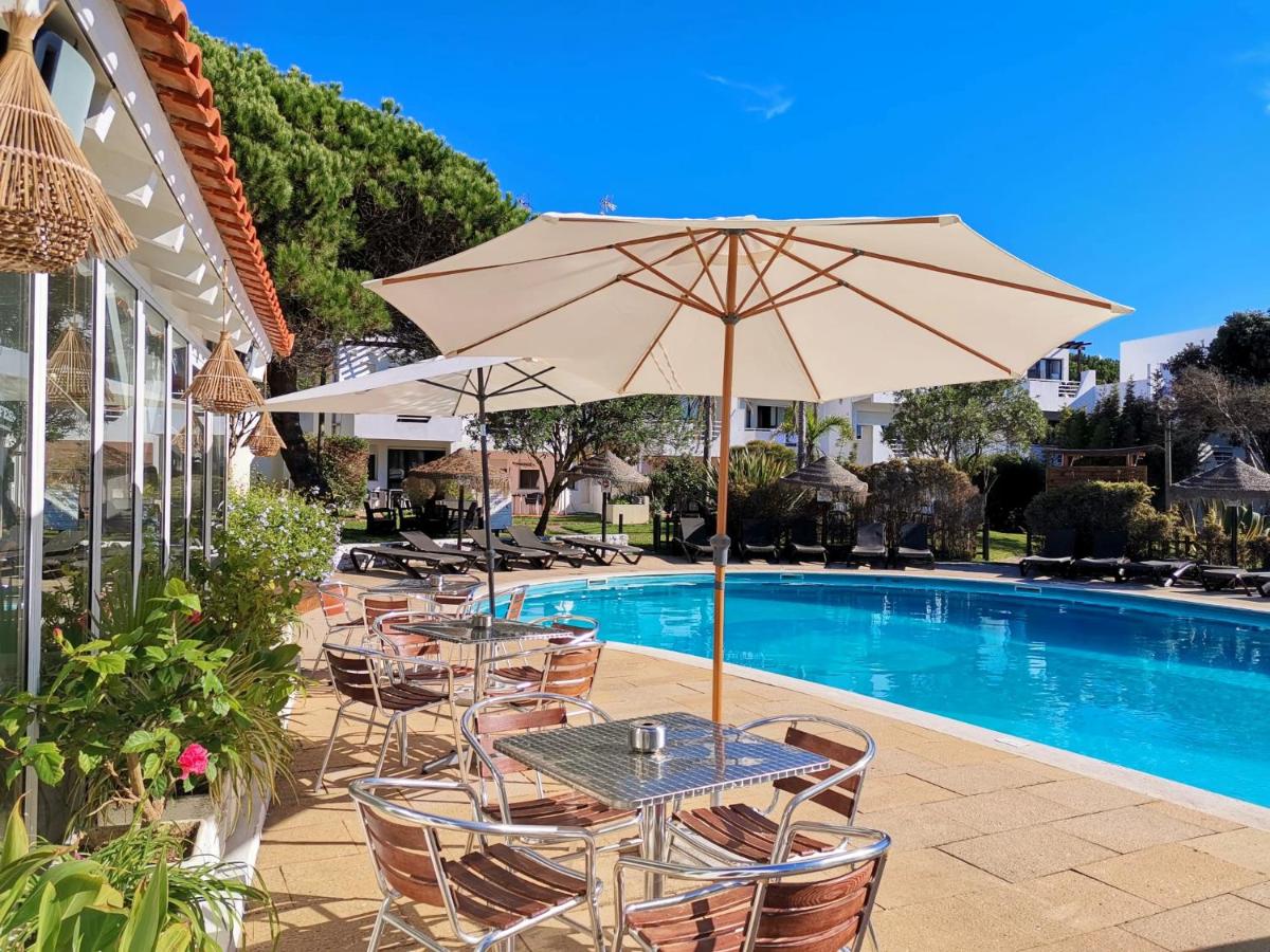 uma mesa e cadeiras com um guarda-sol ao lado da piscina em Duna Parque Beach Club - Duna Parque Group em Vila Nova de Milfontes mais 39 fotografias