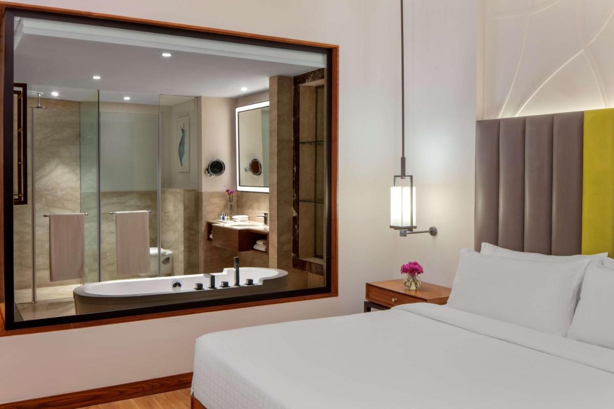 a bedroom with a bed and a bathroom with a tub at Radisson Blu Plaza Hotel Mysore in Mysore