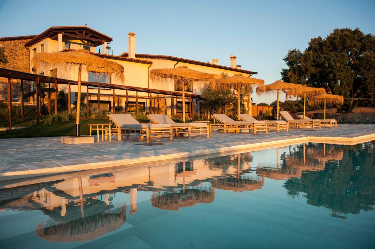 Una piscina con sillas y sombrillas al lado de una casa. en Hábitat Cigüeña Negra, en Valverde del Fresno