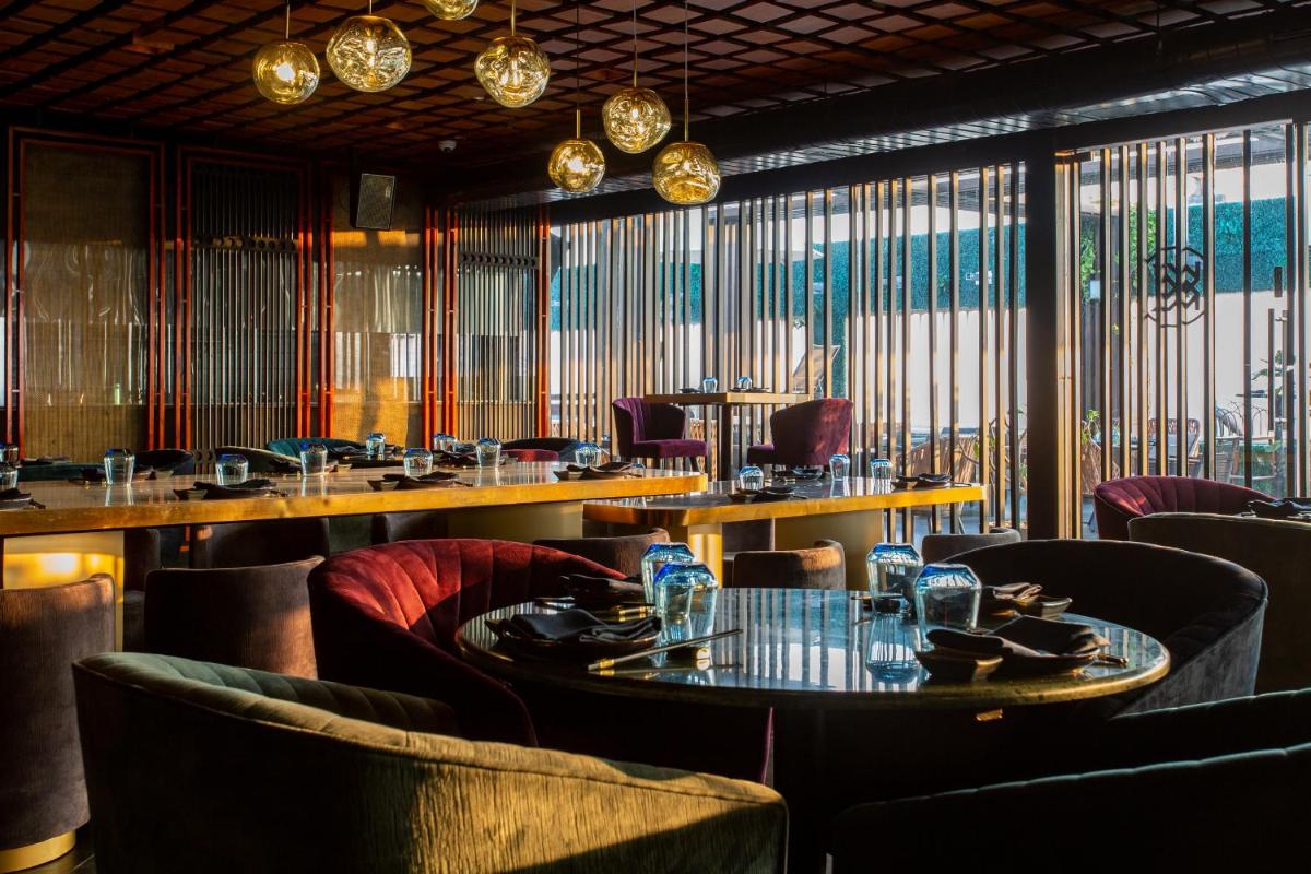 a restaurant with tables and chairs and windows at Novotel Chennai Chamiers Road in Chennai