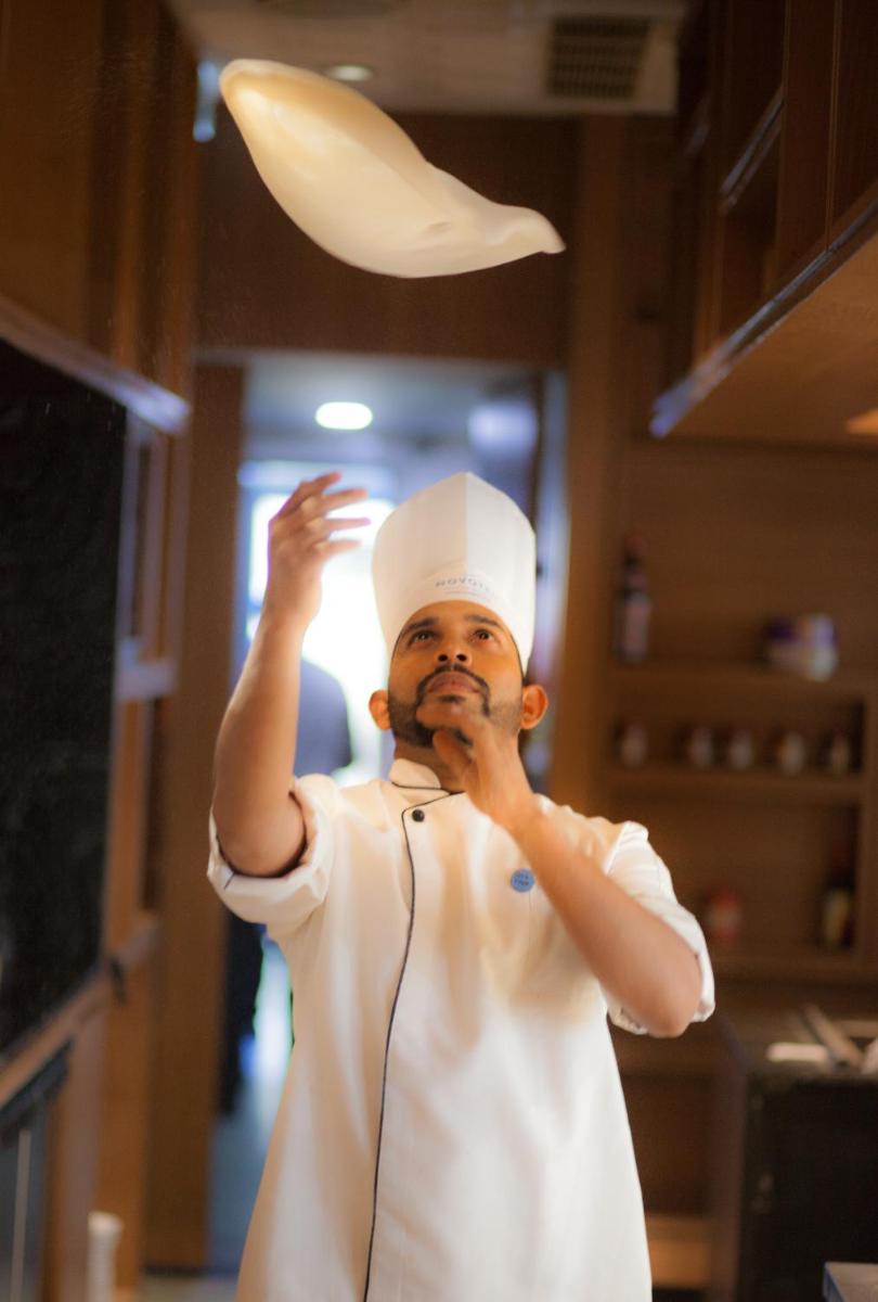 a man wearing a chefs hat holding a chefs hat at Novotel Chennai Chamiers Road in Chennai