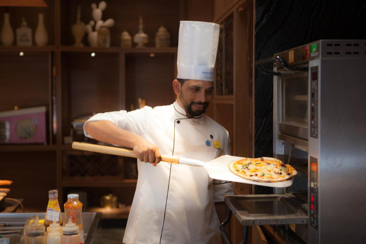 a man in a kitchen holding a pizza on a paddle at Novotel Chennai Chamiers Road in Chennai