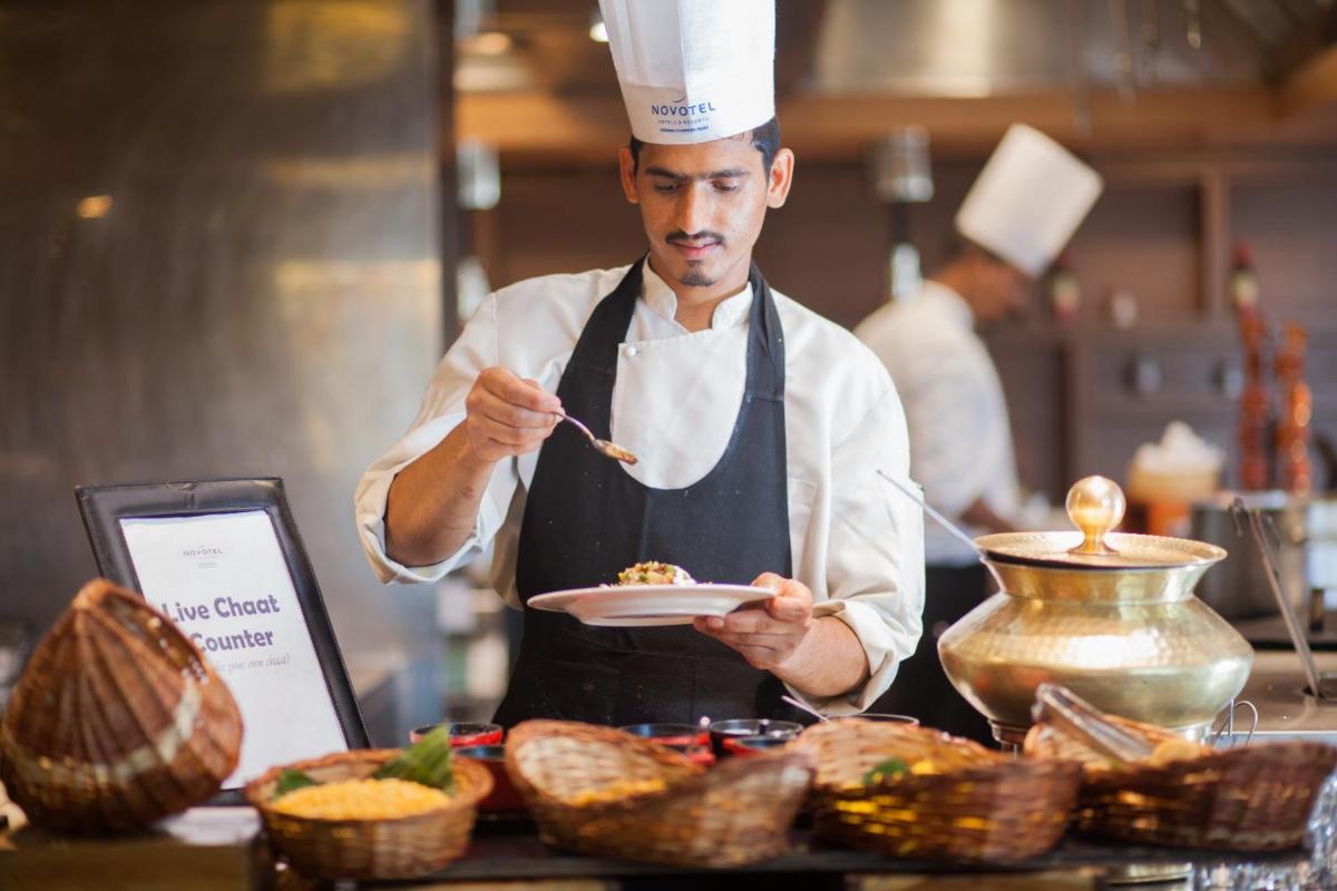 a man in a kitchen holding a plate of food at Novotel Chennai Chamiers Road in Chennai
