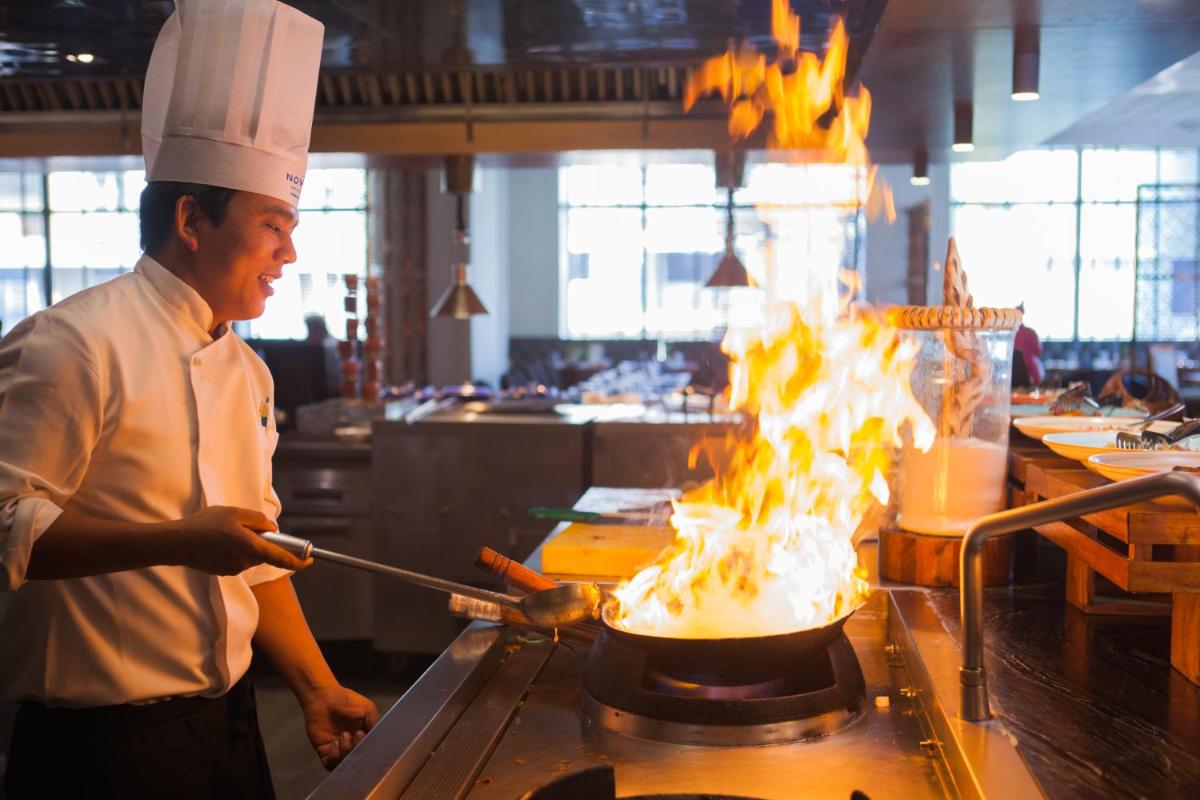 a chef cooking food in a pot on fire at Novotel Chennai Chamiers Road in Chennai