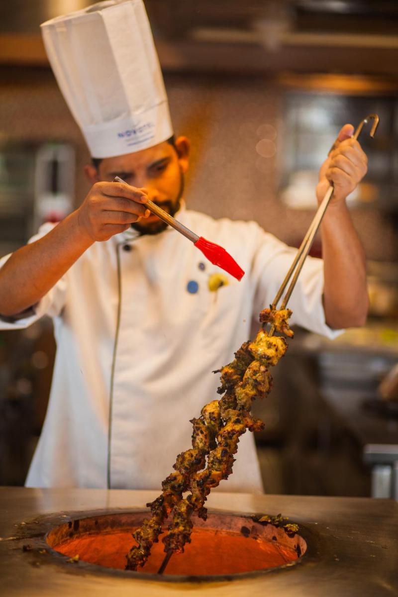 a chef is preparing food in a kitchen at Novotel Chennai Chamiers Road in Chennai