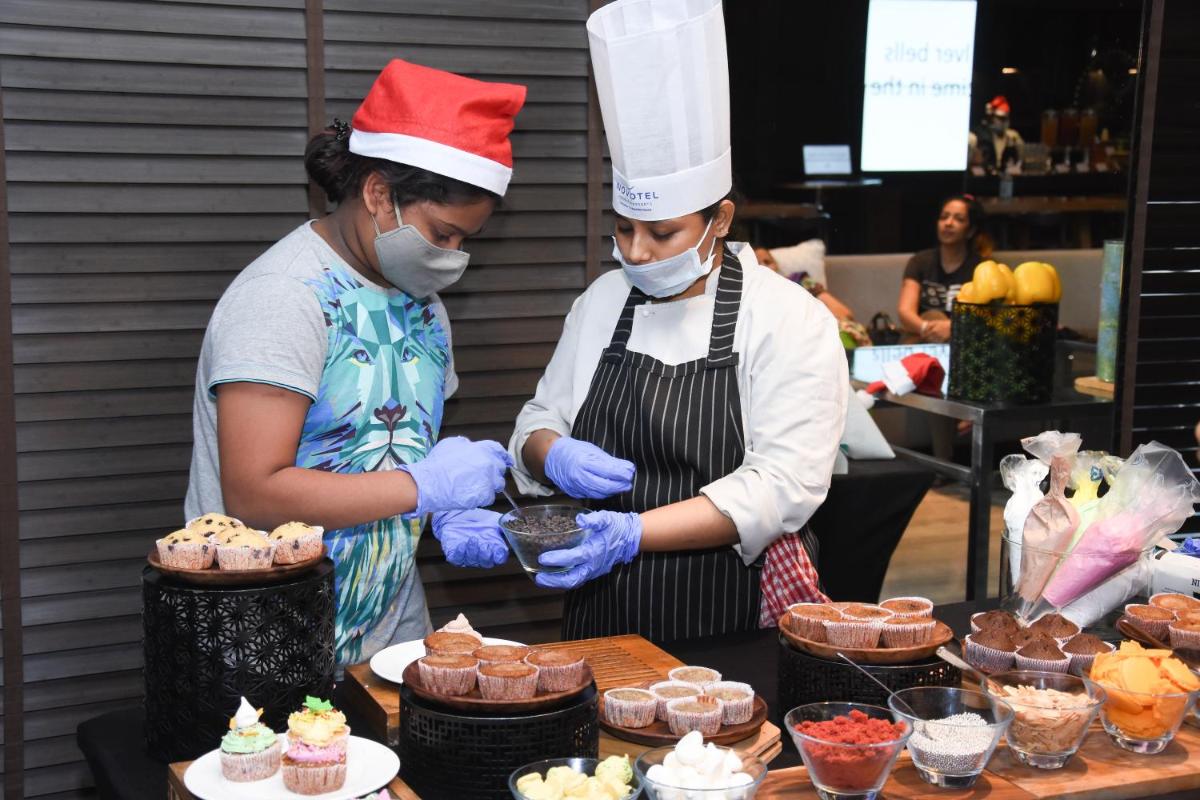 two women wearing masks and hats preparing cupcakes at Novotel Chennai Chamiers Road in Chennai