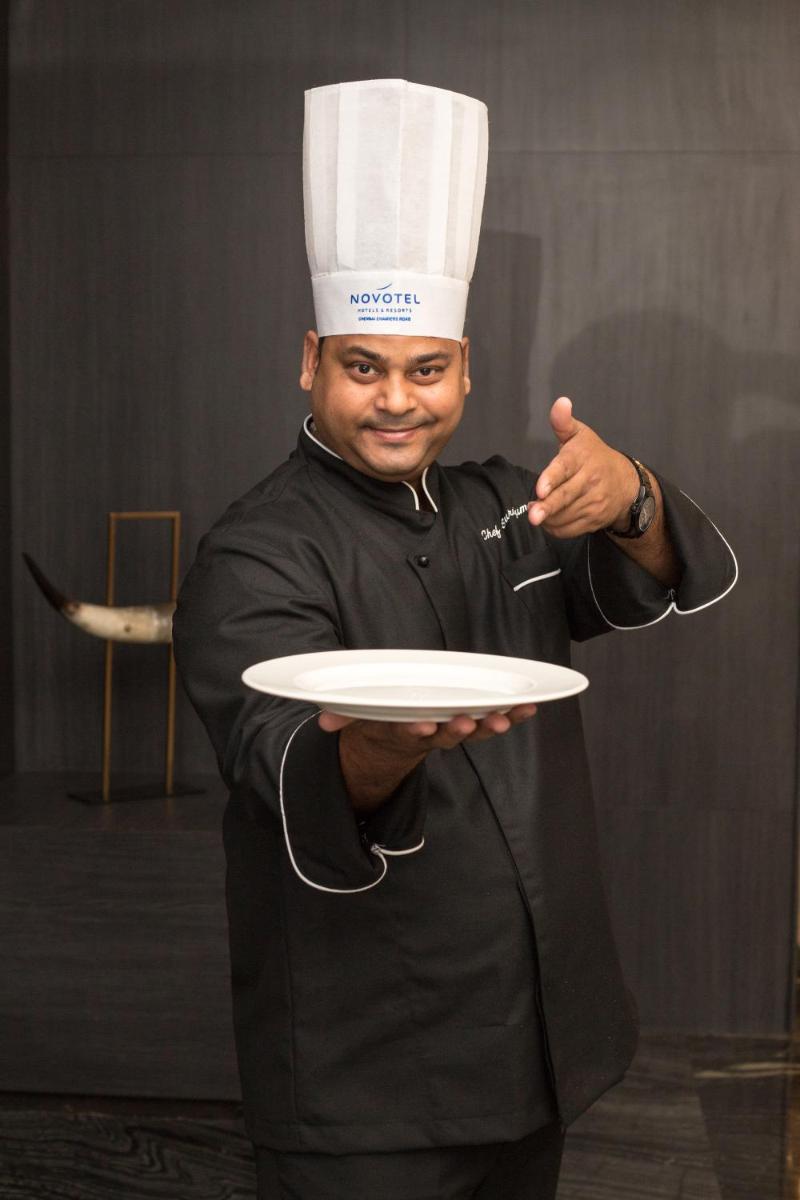 a man wearing a chef hat holding a plate at Novotel Chennai Chamiers Road in Chennai