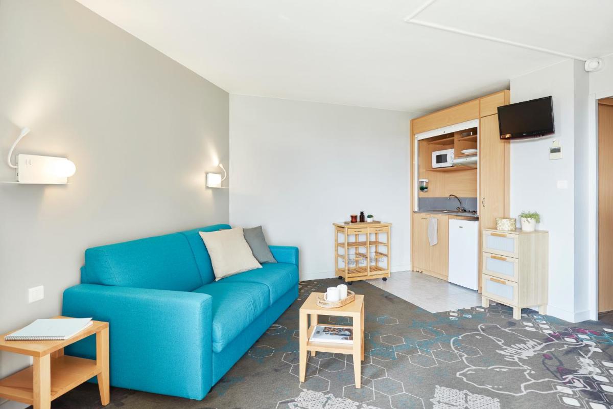 un salon avec un canapé bleu et une cuisine dans l'établissement Résidence Valdys Thalasso & Spa - les Pins, à Saint-Jean-de-Monts