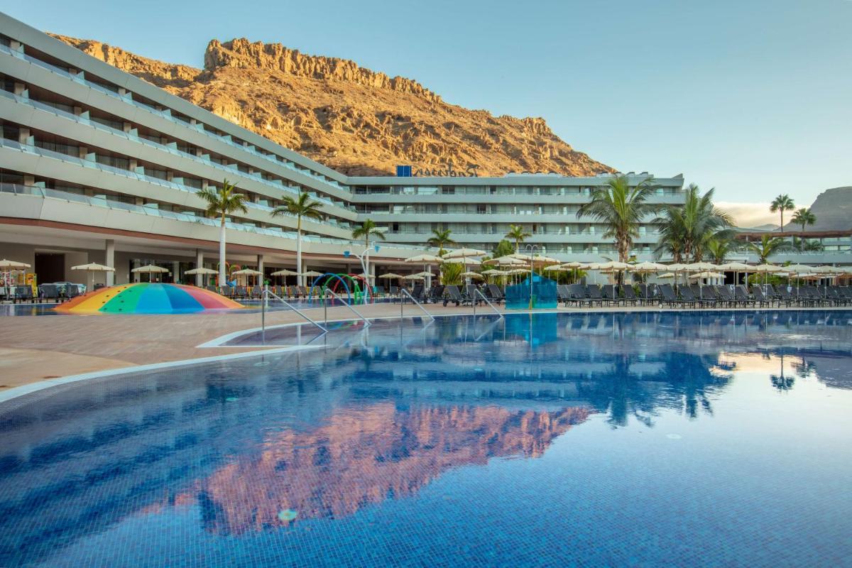 un hotel con una piscina con una montaña en el fondo en Radisson Blu Resort & Spa, Gran Canaria Mogan, en Puerto de Mogán