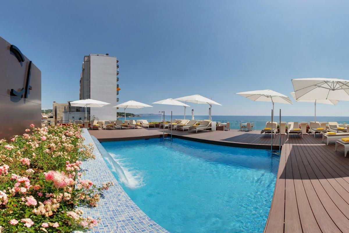 Una piscina con sillas y sombrillas en un edificio. en Cosmopolita Hotel Boutique & Spa, en Platja d'Aro