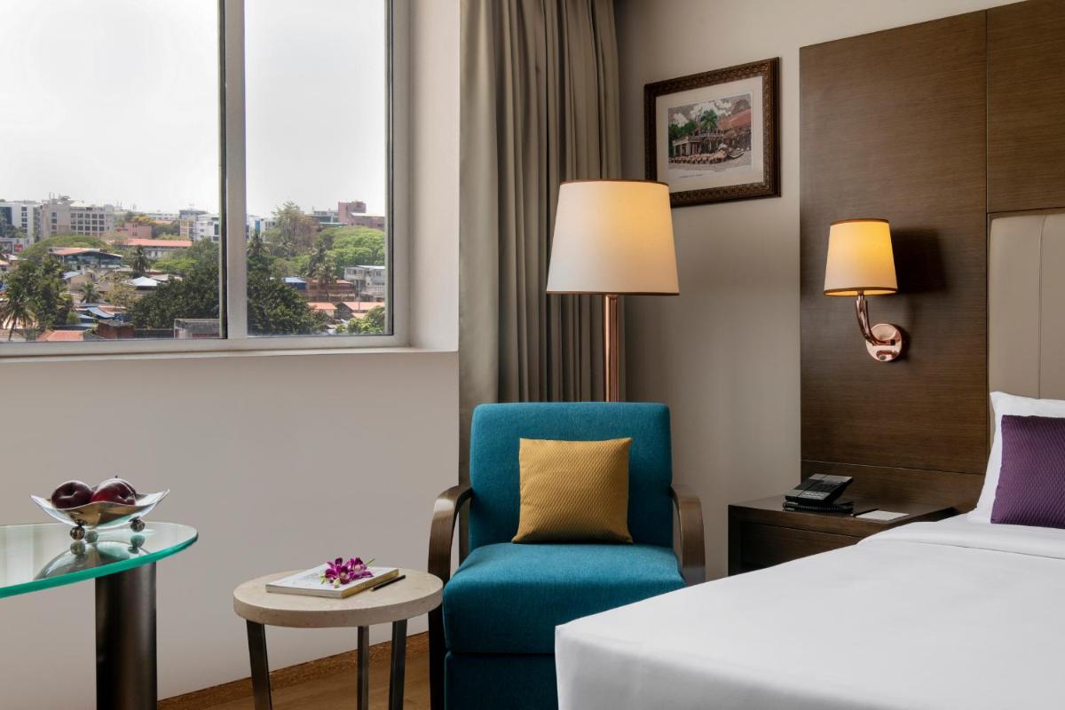 a hotel room with a bed and a chair and a window at Vivanta Thiruvananthapuram in Trivandrum