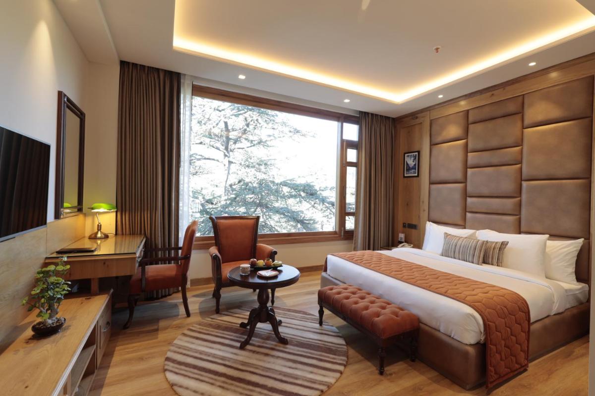 a hotel room with a bed and a desk and a table at WelcomHeritage Elysium Resort & Spa in Shimla