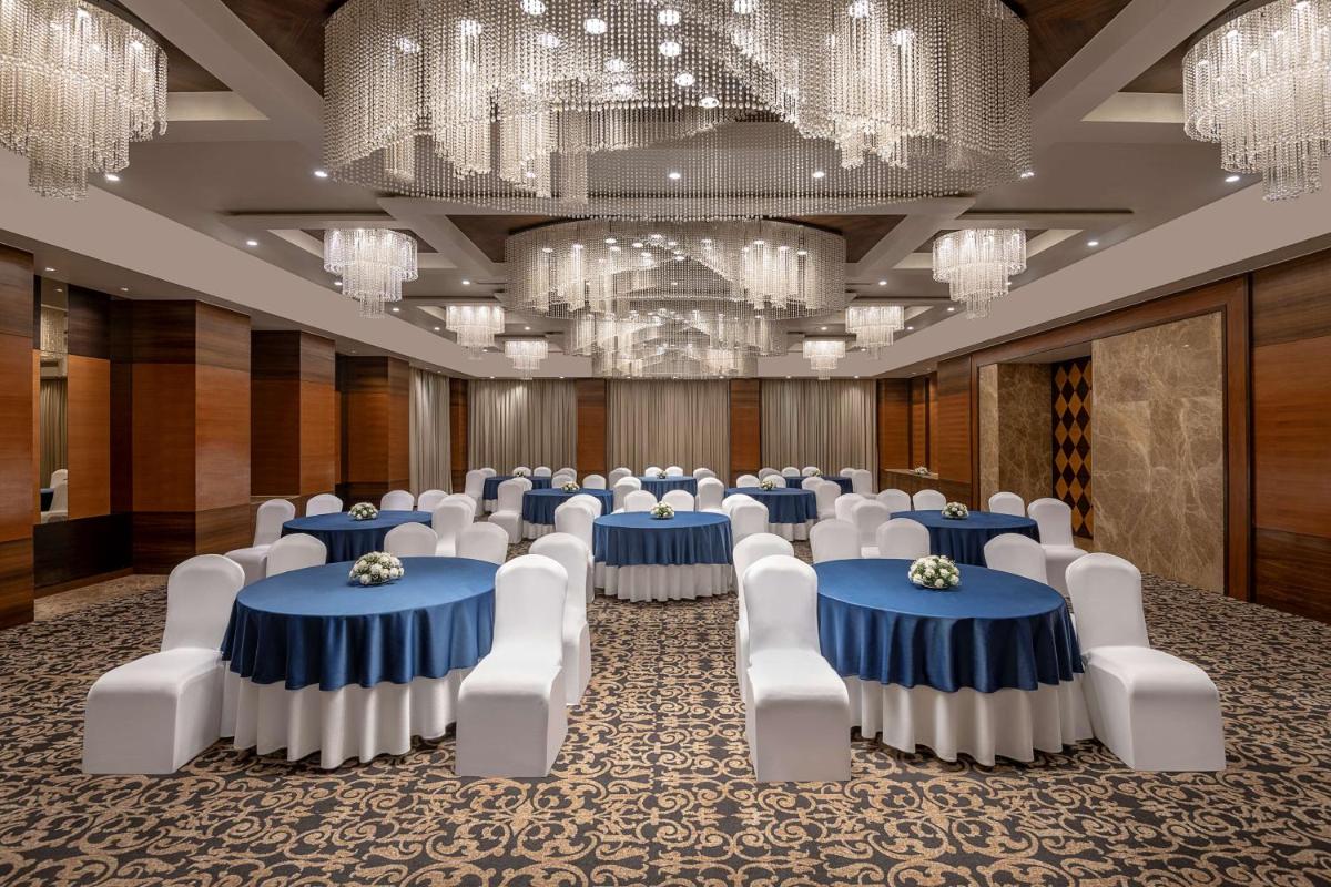 a room with blue tables and white chairs and chandeliers at Radisson Blu Hotel Ahmedabad in Ahmedabad +71 photos