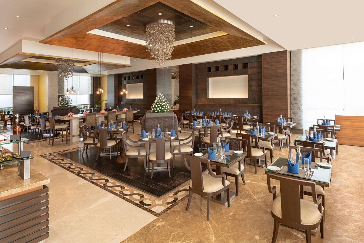 a restaurant with tables and chairs in a room at Radisson Blu Hotel Ahmedabad in Ahmedabad