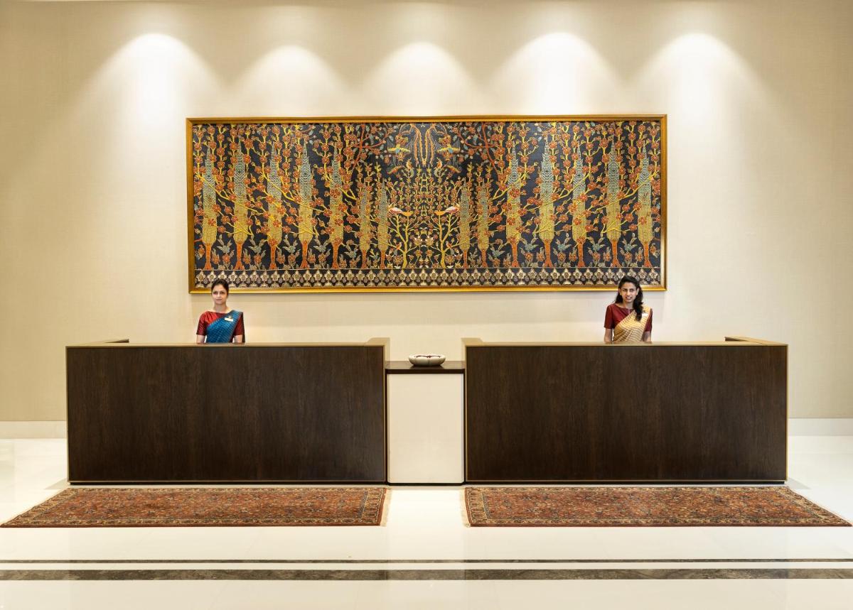 two women sitting at reception desks in a museum with a painting at The Leela Bhartiya City Bengaluru in Bengaluru two women sitting at reception desks in a museum with a painting at The Leela Bhartiya City Bengaluru in Bengaluru