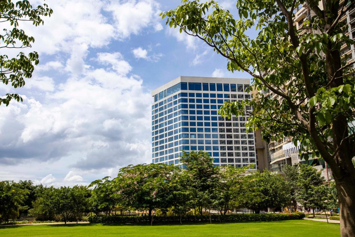 a tall blue building with trees in front of it at The Leela Bhartiya City Bengaluru in Bengaluru a tall blue building with trees in front of it at The Leela Bhartiya City Bengaluru in Bengaluru