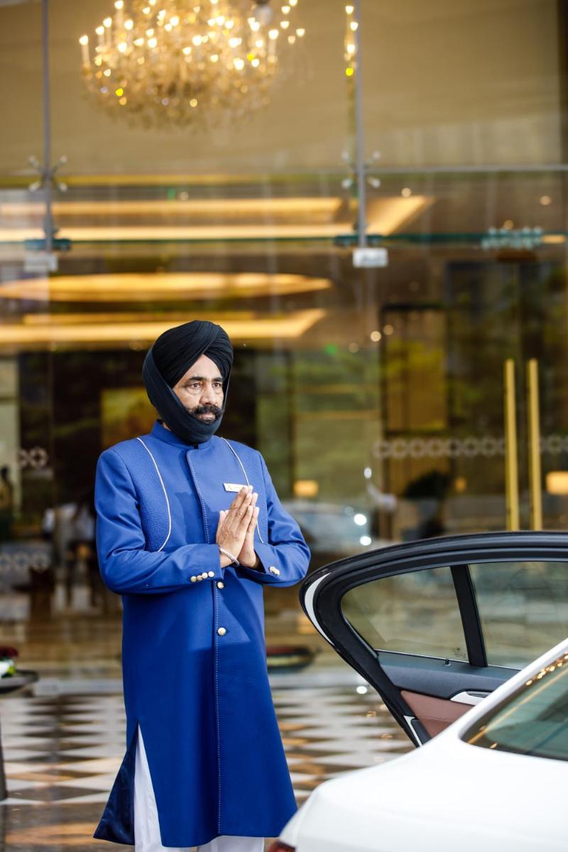 a man in a blue coat standing next to a car at The Leela Bhartiya City Bengaluru in Bengaluru a man in a blue coat standing next to a car at The Leela Bhartiya City Bengaluru in Bengaluru