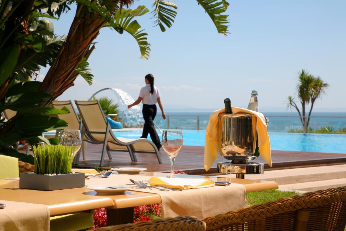 uma mesa com taças de vinho e uma pessoa caminhando perto de uma piscina em Hotel Cascais Miragem Health & Spa em Cascais