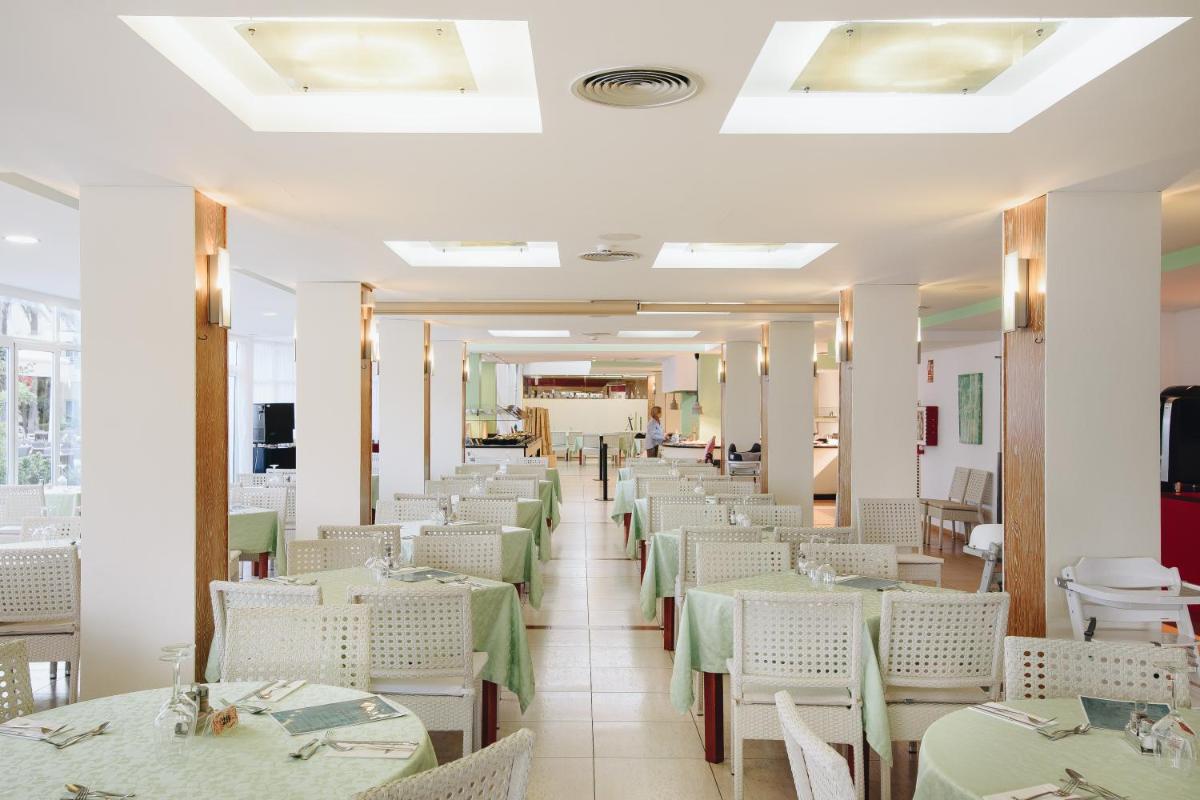 Un comedor con mesas verdes y sillas blancas. en Hotel Ivory Playa Sports & Spa, en Puerto de Alcudia
