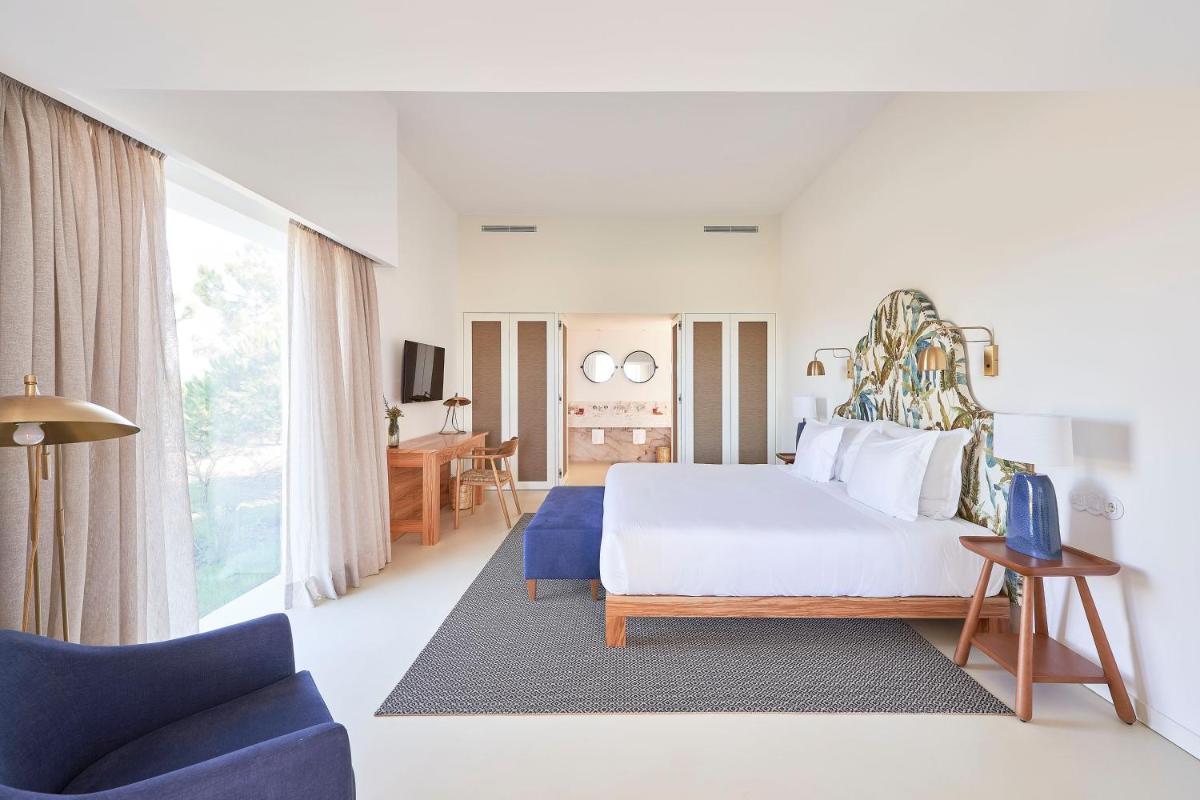 um quarto com uma cama branca e uma cadeira azul em Praia do Canal Nature Retreat - Small Luxury Hotels of the World em Aljezur mais 100 fotografias