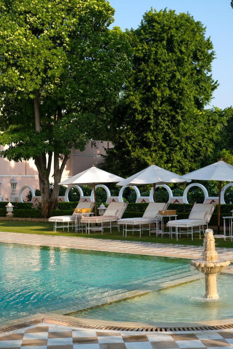 a pool with chairs and umbrellas and a fountain at Rajmahal Palace RAAS in Jaipur