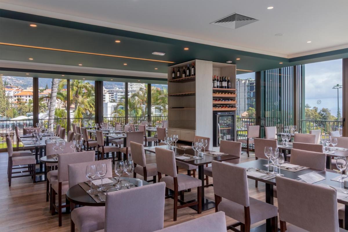 um restaurante com mesas, cadeiras e janelas em Enotel Magnólia no Funchal