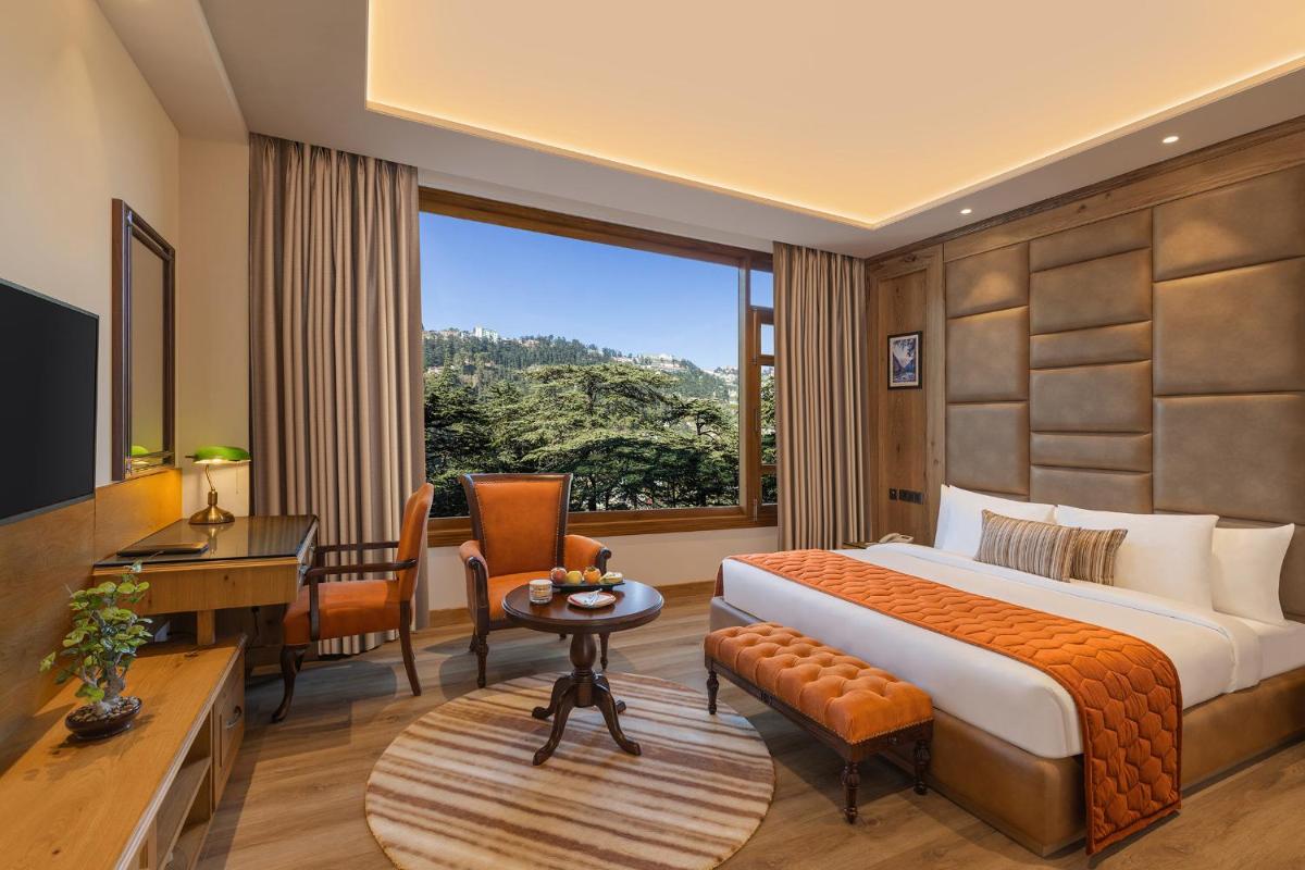 a hotel room with a bed and a desk and a window at WelcomHeritage Elysium Resort & Spa in Shimla