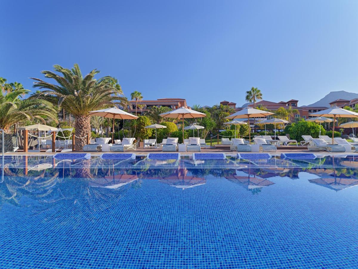 Una piscina con sillas y sombrillas en un resort. en H10 Costa Adeje Palace, en Adeje