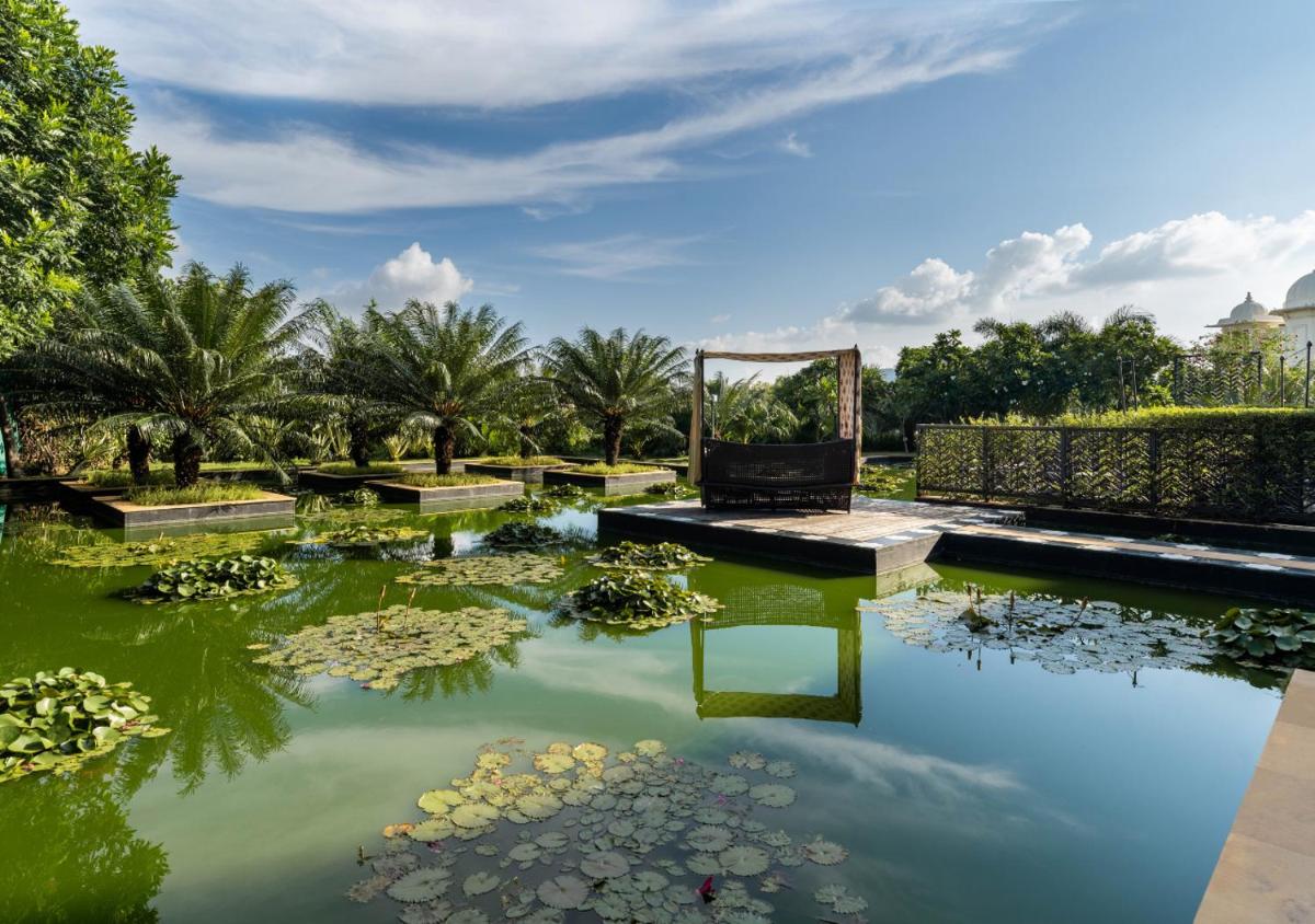 a pond with a bench and lilies in a park at The Leela Palace Udaipur in Udaipur