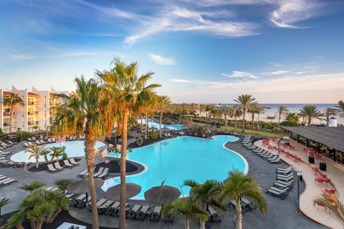 Una vista aérea de la piscina de un resort con palmeras y sillas. en Barceló Fuerteventura Mar, en Caleta de Fuste