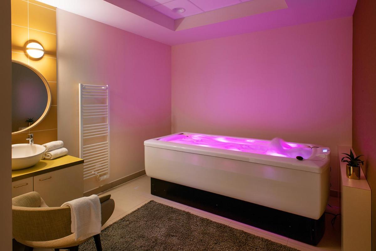 La salle de bains est pourvue d'une baignoire avec un mur violet. dans l'établissement Le Critérium, à Écouflant