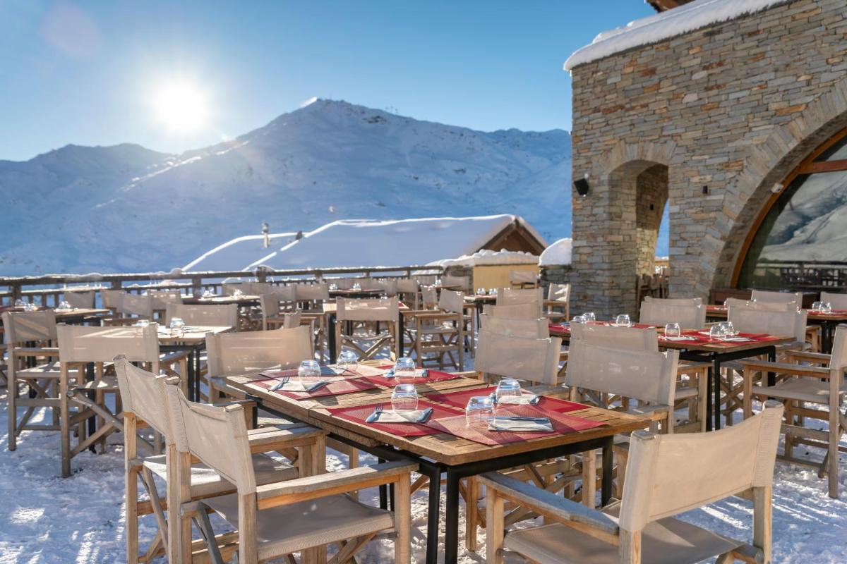 une table et des chaises avec une montagne en arrière-plan dans l'établissement Chalet Hotel Kaya, aux Menuires