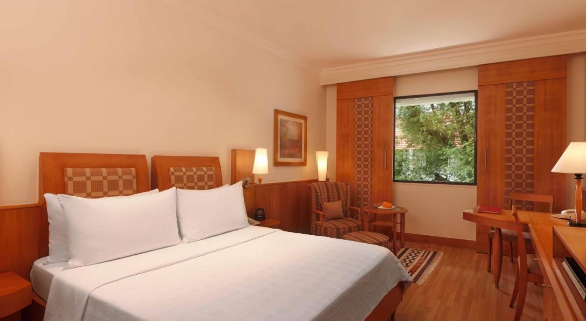 a bedroom with a bed and a desk and a window at Trident Chennai in Chennai