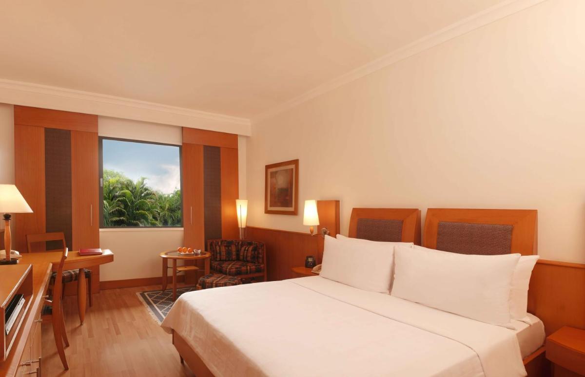 a hotel room with a bed and a desk and a window at Trident Chennai in Chennai
