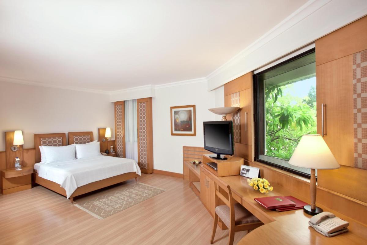a bedroom with a bed and a desk with a television at Trident Chennai in Chennai