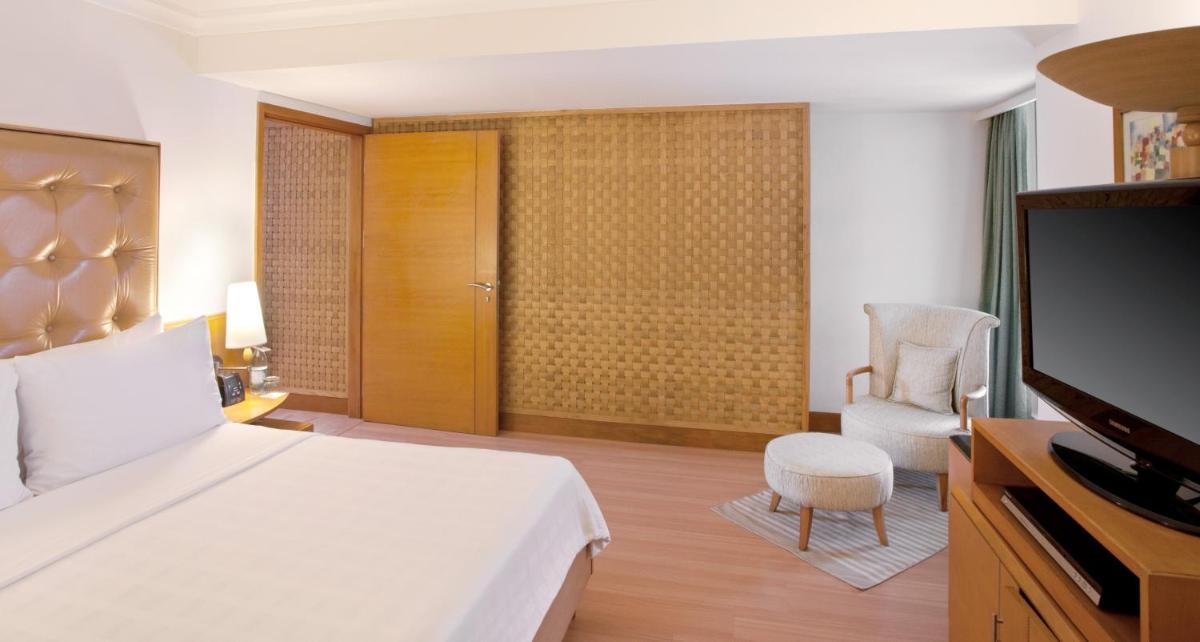 a bedroom with a bed and a tv and a chair at Trident Chennai in Chennai