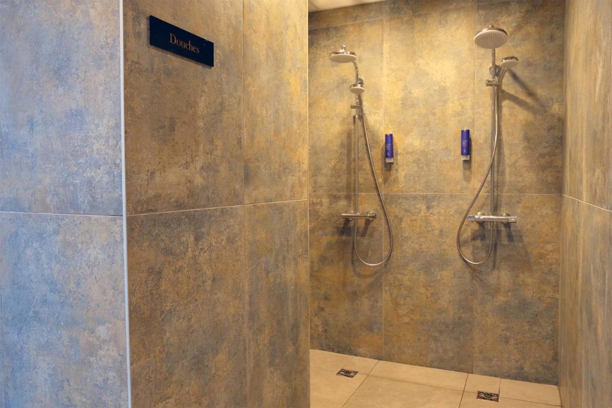 une salle de bain avec douche avec un panneau sur le mur dans l'établissement Madame Vacances Hôtel & Spa Le Mottaret, à Méribel