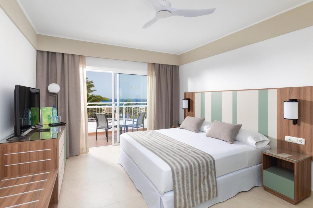 Un dormitorio con una cama y un televisor y un balcón. en Hotel Riu Paraiso Lanzarote - All Inclusive, en Puerto del Carmen