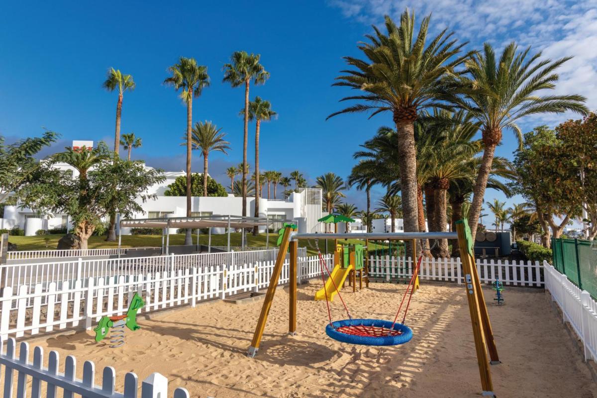 Un parque infantil en la arena con palmeras en Hotel Riu Paraiso Lanzarote - All Inclusive, en Puerto del Carmen